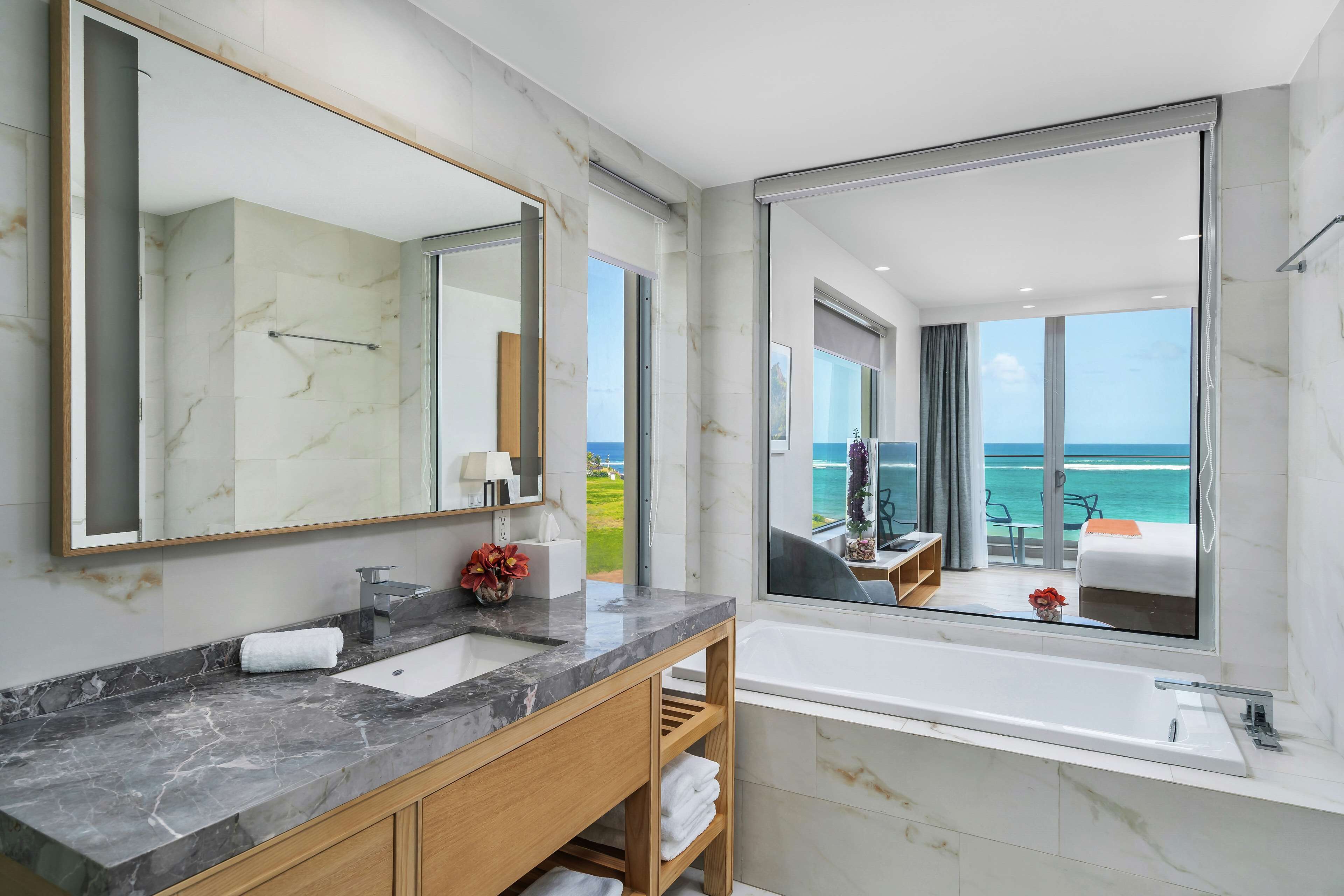 Une salle de bain moderne avec un comptoir en marbre, un grand miroir et une vue sur l’océan par une grande fenêtre.