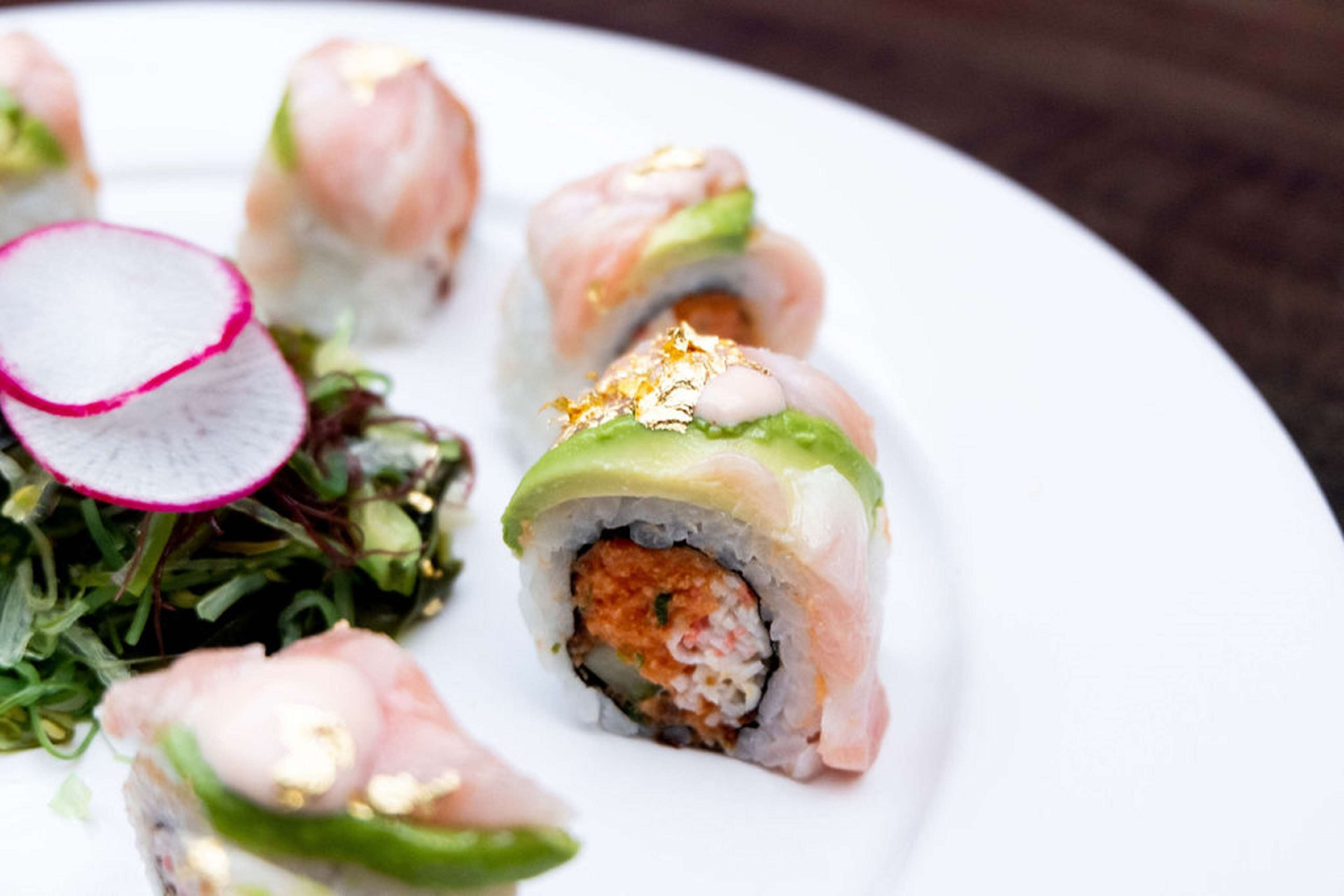 A plate with sushi rolls, a radish slice, and a green leafy salad.