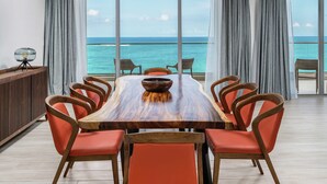 A dining area with a large wooden table, red chairs, and a view of the ocean through large windows. - Koi Resort Saint Kitts, Curio Collection by Hilton (Basseterre)