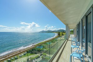 A balcony with a view of the ocean and beach, featuring glass railings and blue chairs. - Koi Resort Saint Kitts, Curio Collection by Hilton (Basseterre)