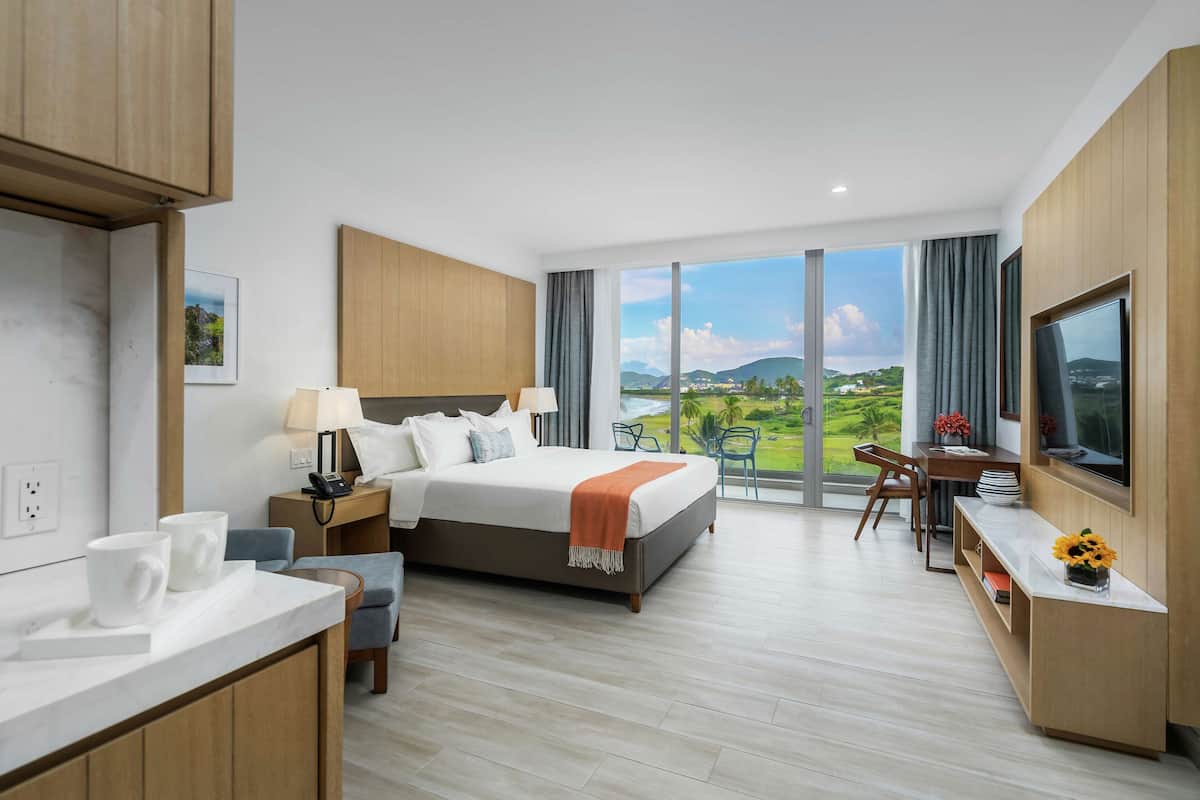 A modern hotel room with a large bed, a desk, and a view of a green landscape.