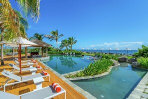 A pool area with lounge chairs and umbrellas, surrounded by palm trees and a view of the ocean. - Koi Resort Saint Kitts, Curio Collection by Hilton (Basseterre)