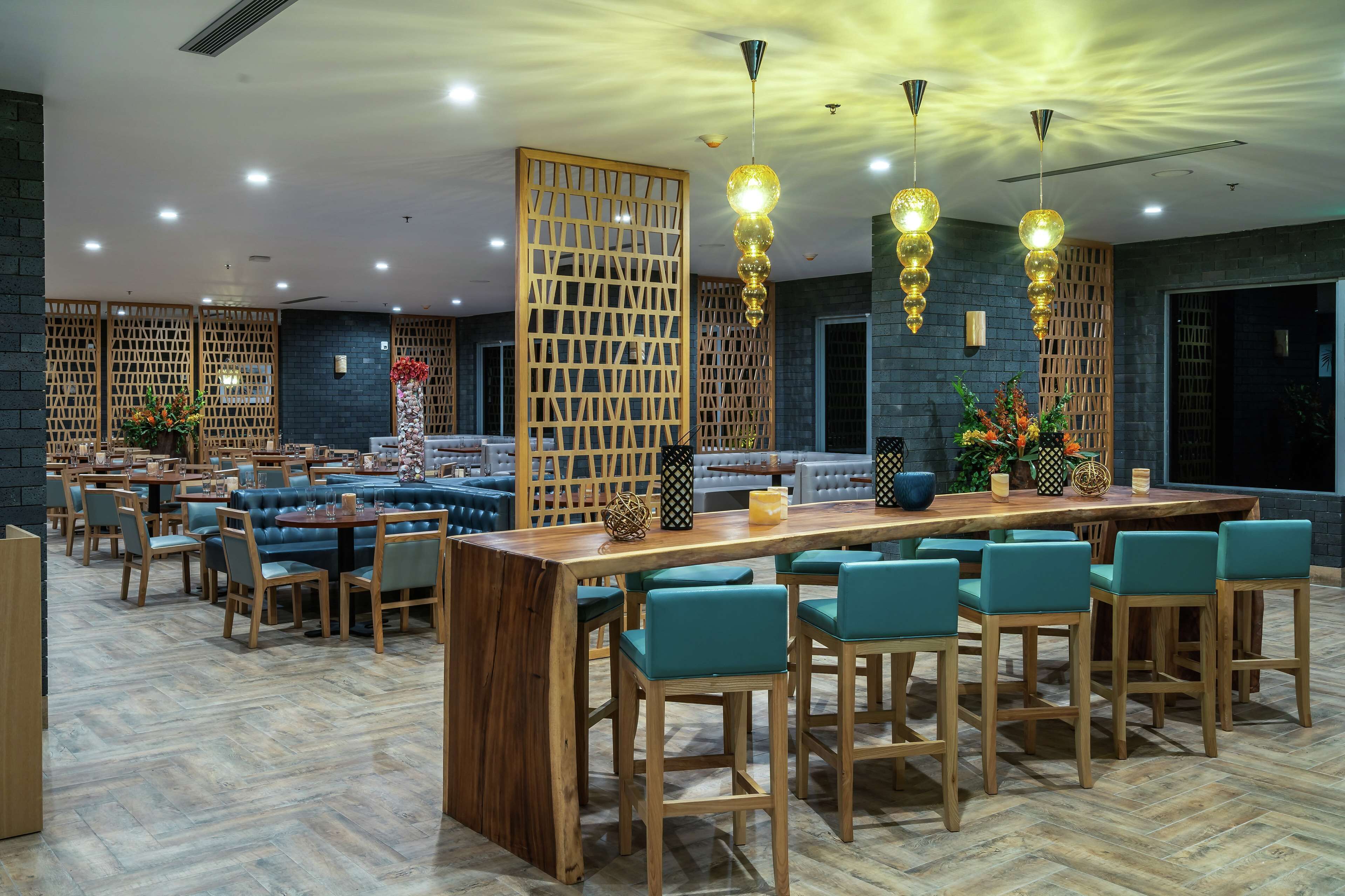 Un restaurant modern amb mobles de fusta, una zona de bar central i il·luminació decorativa.