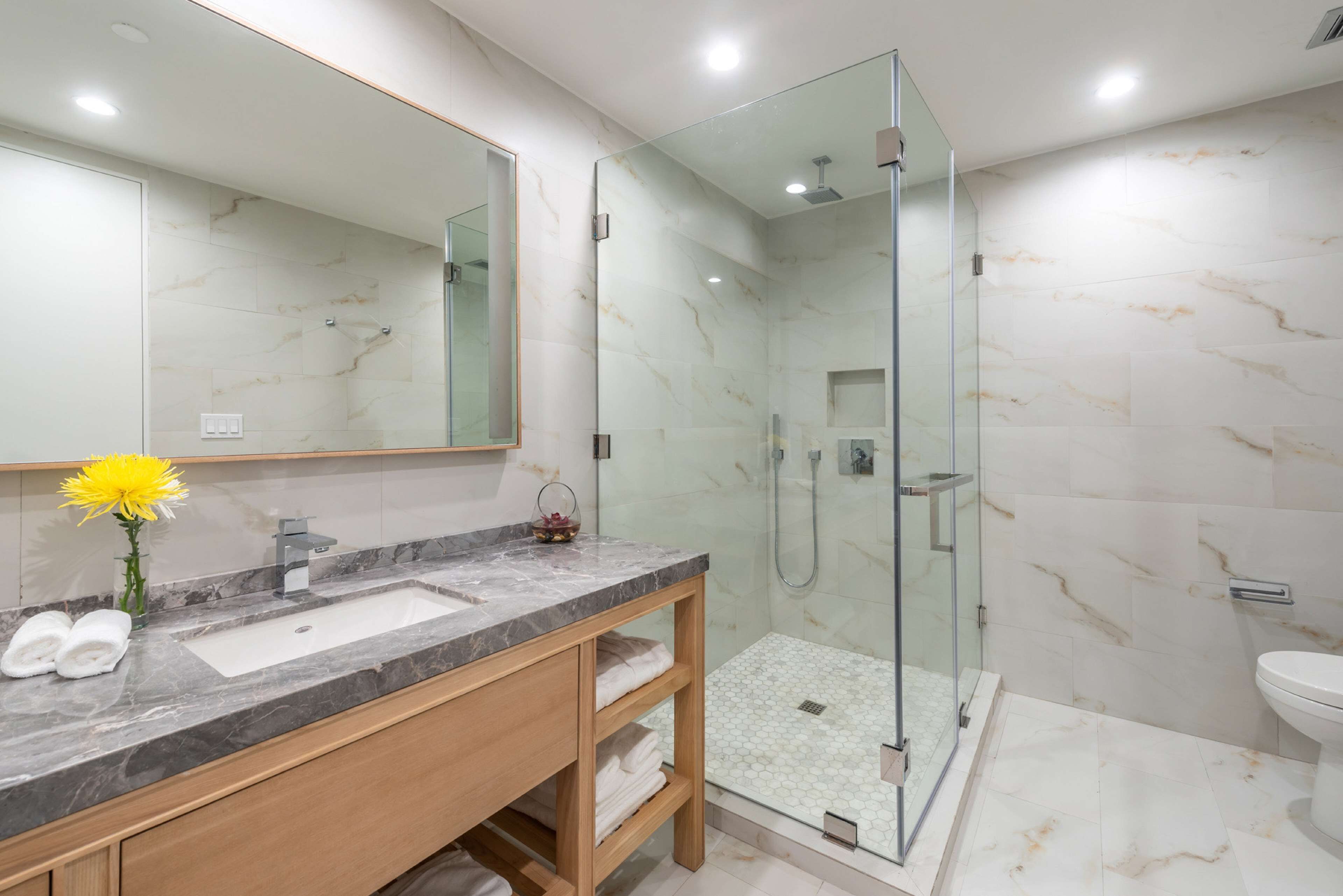 A modern bathroom with a marble sink, glass shower enclosure, and a large mirror.