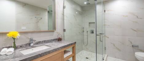 A modern bathroom with a marble sink, glass shower enclosure, and a large mirror.