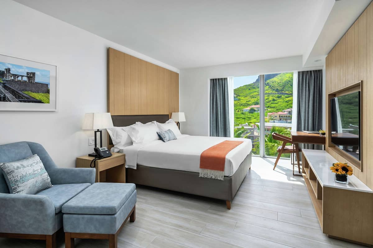 A modern hotel room with a large bed, a desk, a chair, and a TV.