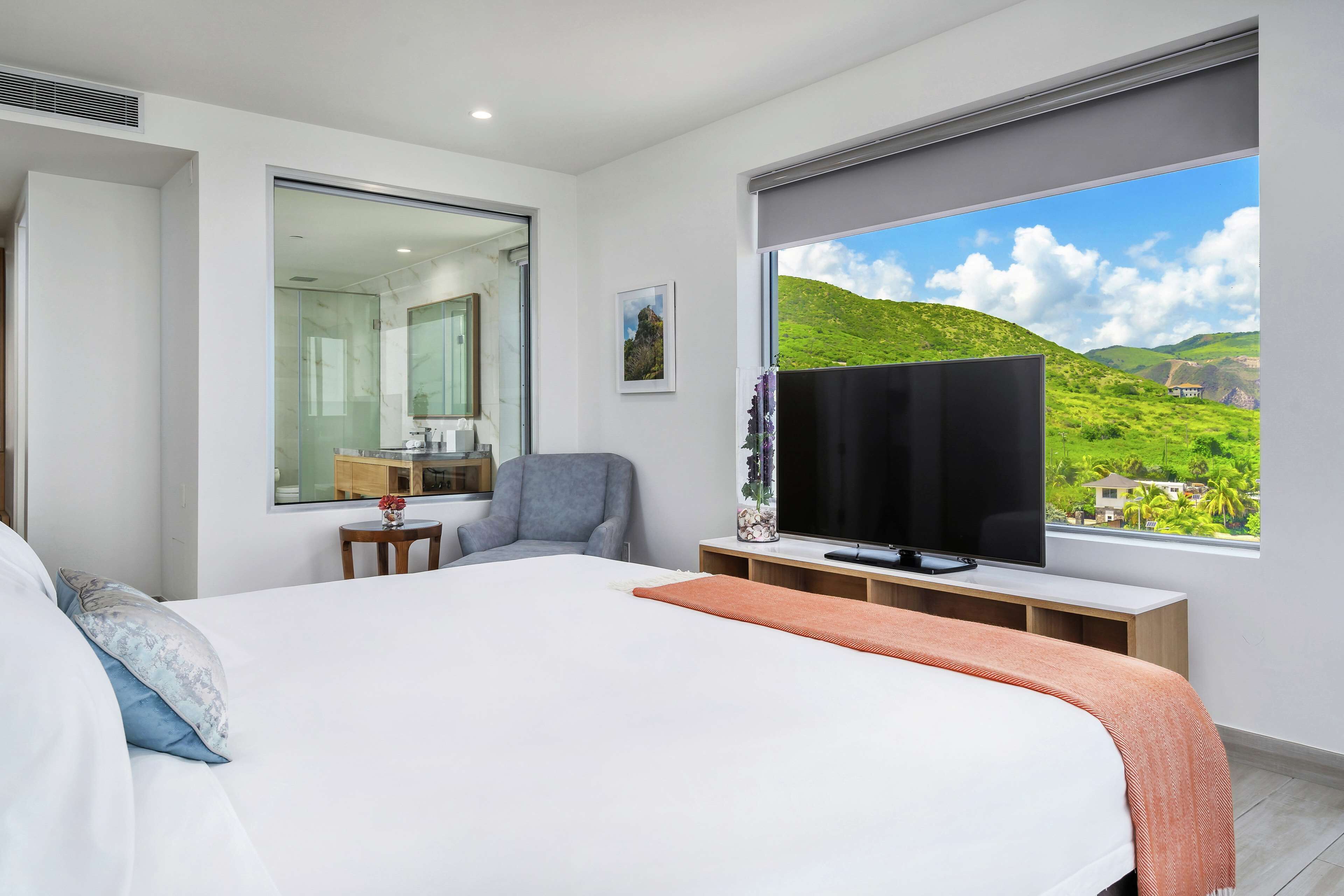 Een moderne hotelkamer met een groot bed, een televisie, een bureau en een raam met uitzicht op glooiende groene heuvels.