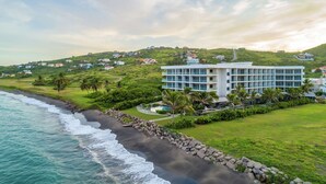 A coastal hotel with a modern design, featuring a large building with multiple balconies, a private beach, and lush greenery. - Koi Resort Saint Kitts, Curio Collection by Hilton (Basseterre)