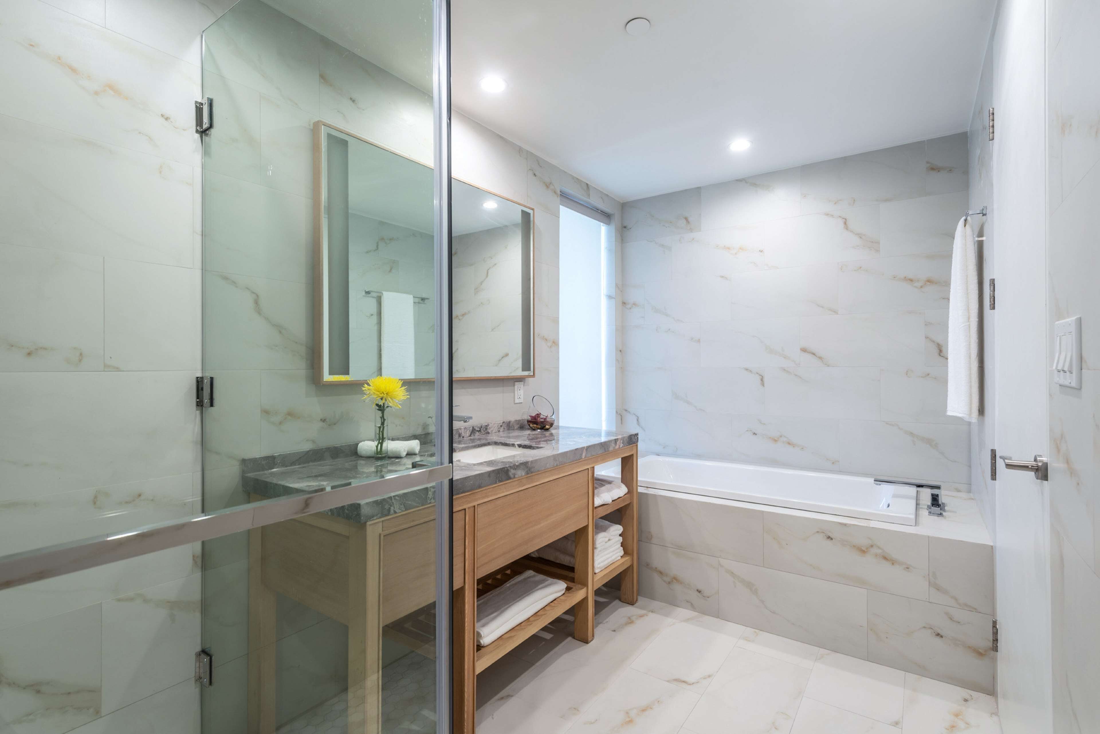 Un baño moderno con cabina de ducha de vidrio, tocador de madera, un espejo grande y una bañera.