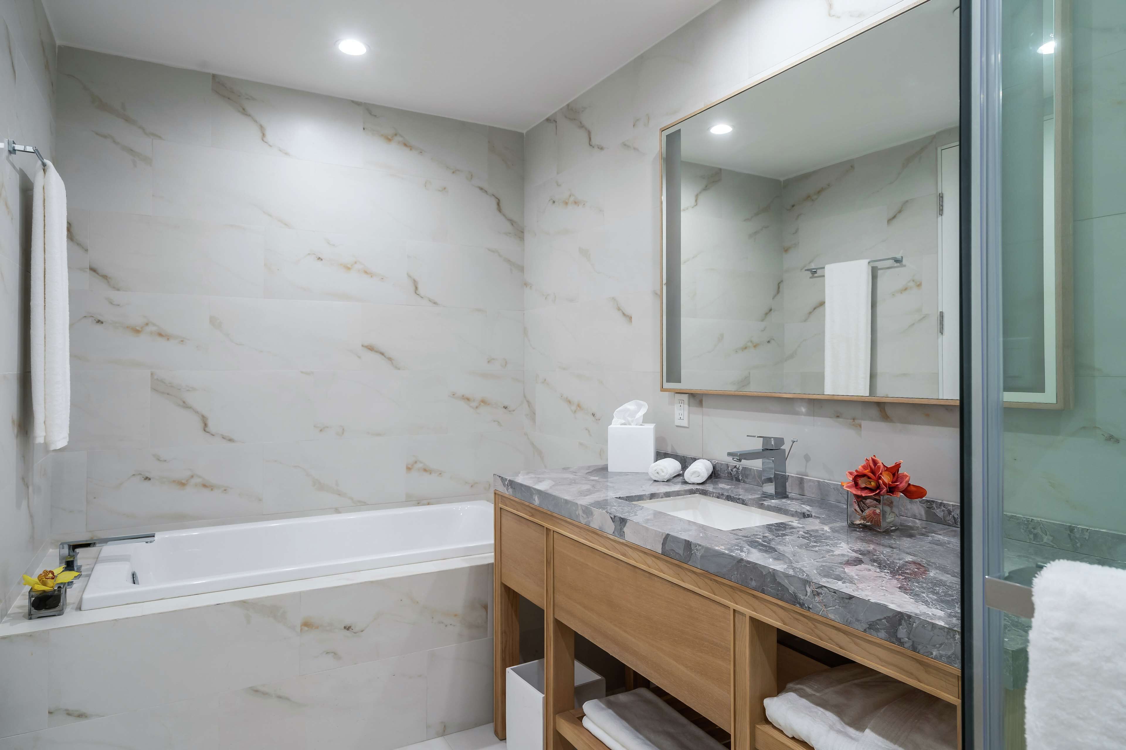 A modern bathroom with marble walls, a bathtub, a vanity with a sink, and a large mirror.