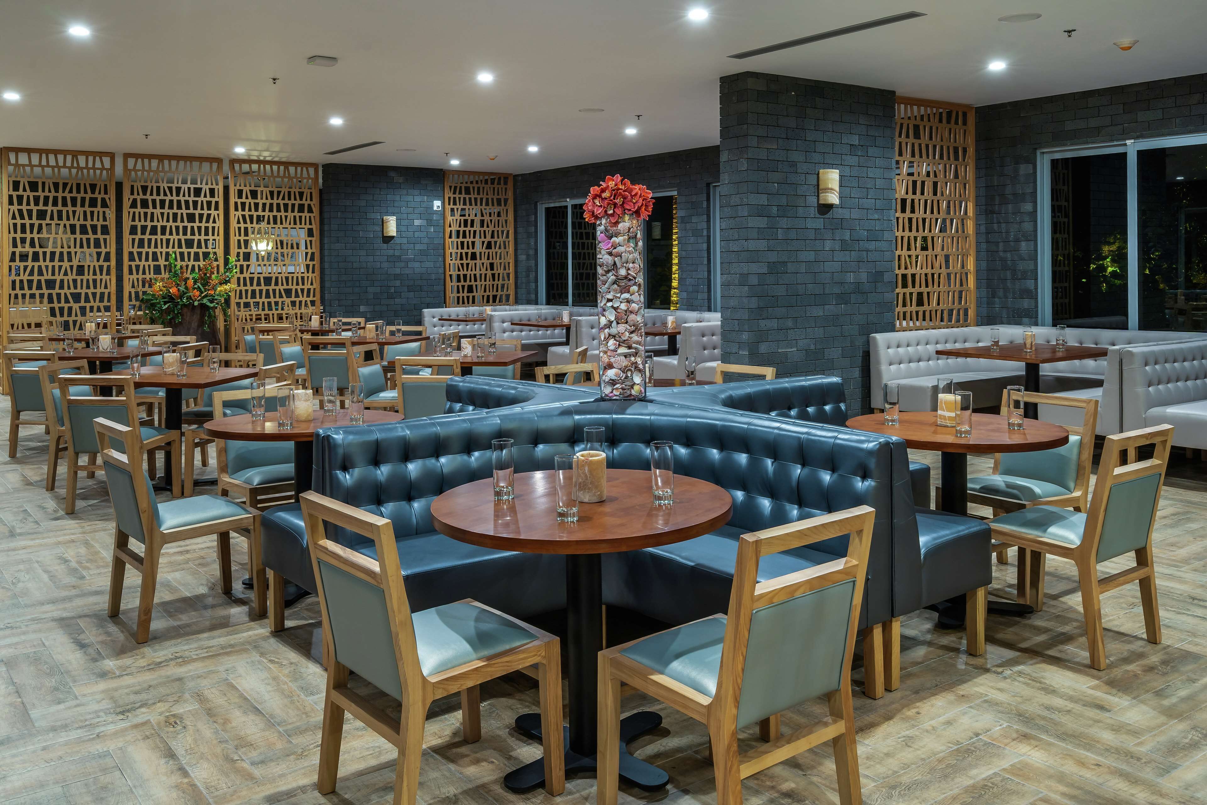 A modern restaurant with round tables, blue cushioned seating, and a decorative vase.