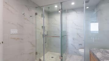 Ein modernes Badezimmer mit einer gläsernen Duschkabine, Marmorfliesen und einem sichtbaren WC.