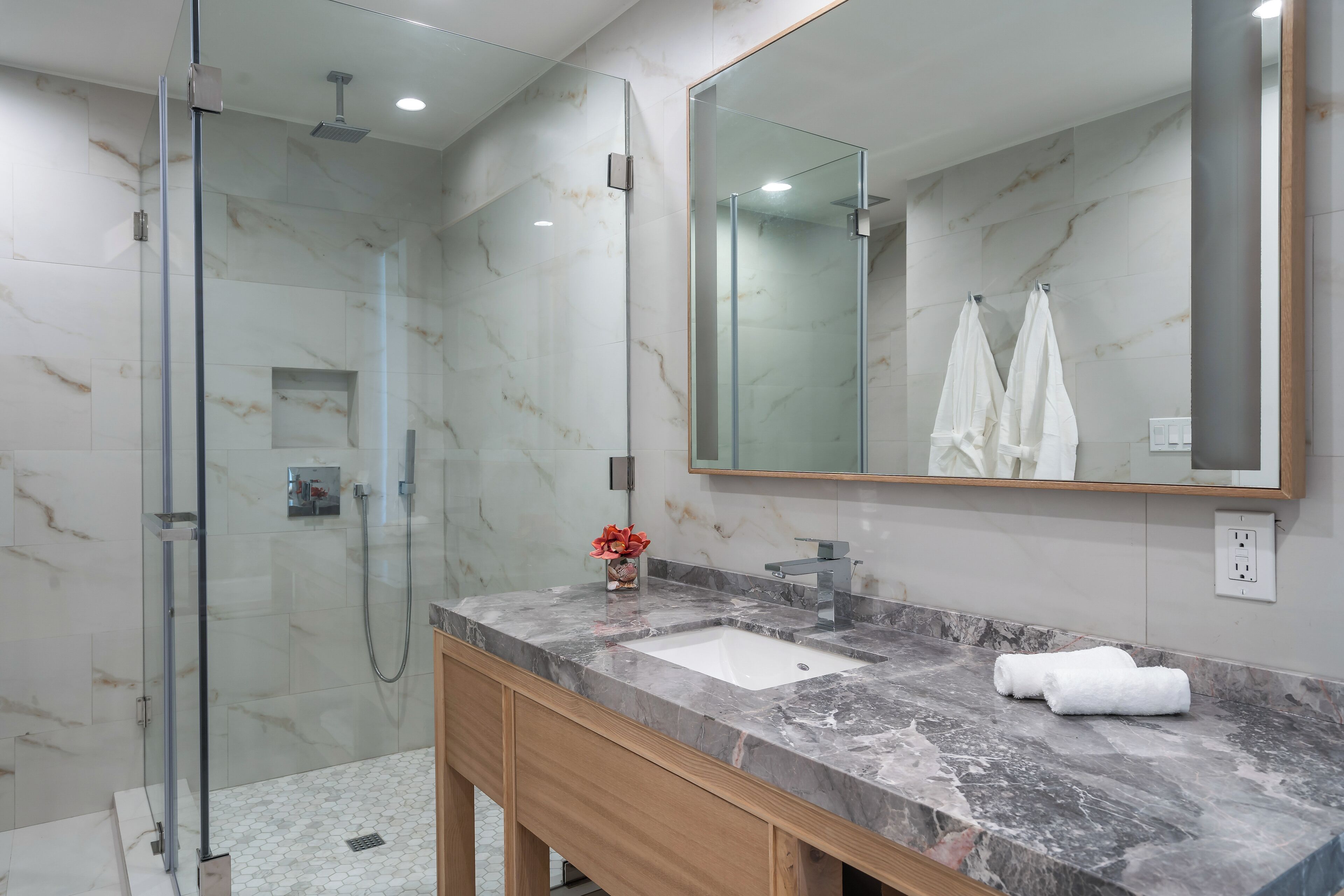 A modern bathroom with a glass-enclosed shower, a marble sink, and a large mirror.