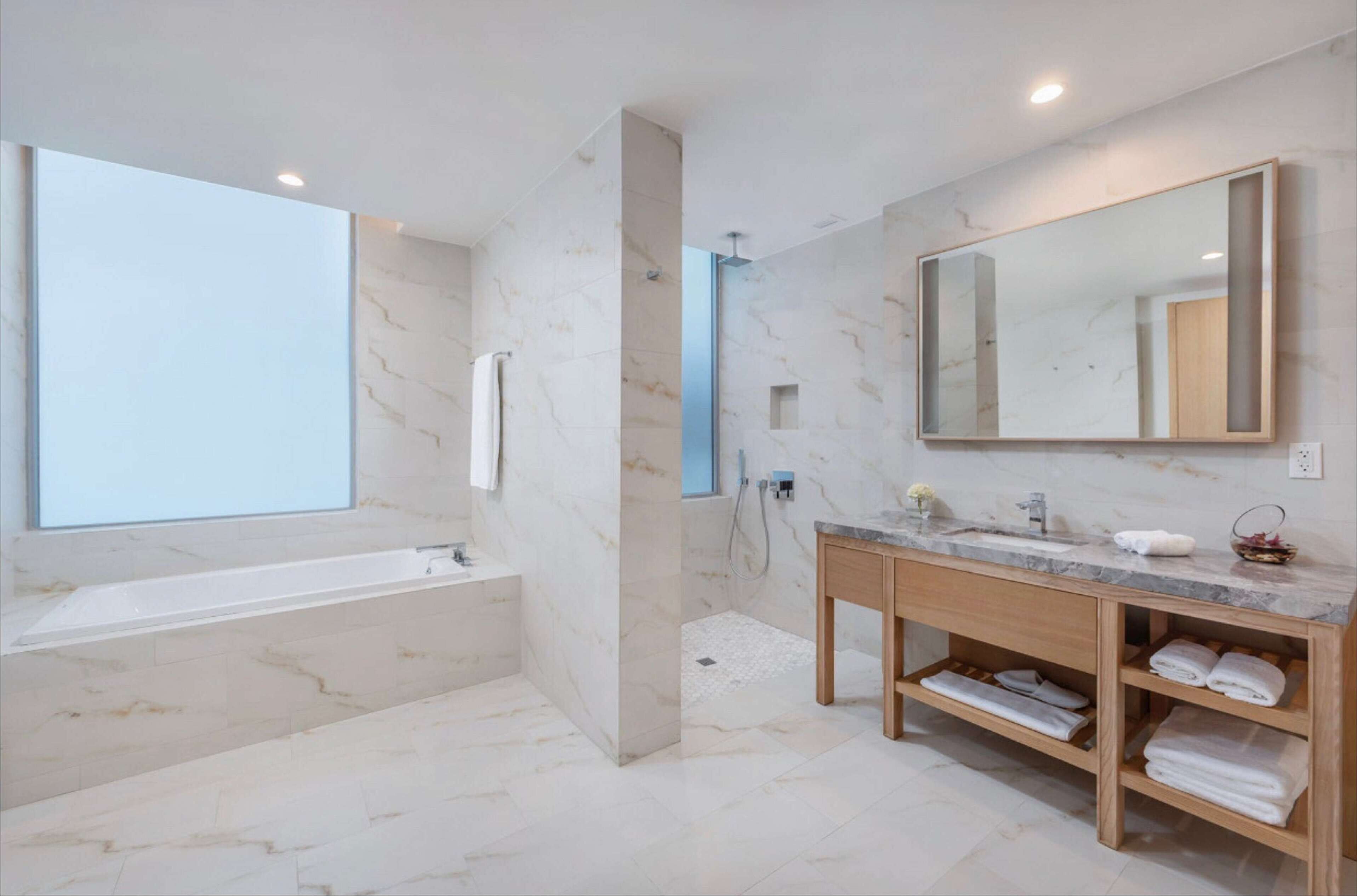 Un baño moderno con suelo de mármol, un espejo grande, un tocador de madera y una bañera.