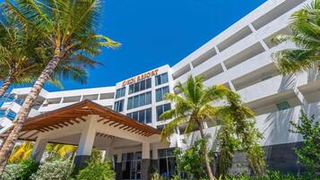 A modern hotel with a white facade, multiple balconies, and a covered entrance area with palm trees.