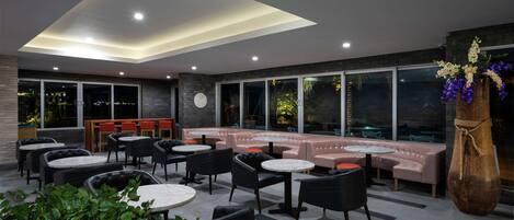 A modern indoor seating area with round tables and black chairs, a pink sofa, and a large vase of flowers.