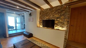 Un salon avec un mur en pierre, un téléviseur, un banc en bois et un tapis à motifs.