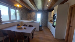Une cuisine compacte avec un mur en pierre, des poutres en bois, une table à manger avec des chaises et une vue par la fenêtre.