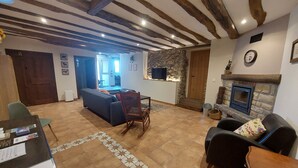 Un salon avec une cheminée, un canapé, une table à manger avec des chaises, et un coin cuisine à l’arrière-plan.