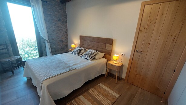 Une chambre à coucher avec un lit, des lampes de chevet, une tête de lit en bois, une porte en bois et un mur en pierre.