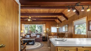 Amplia sala de estar con techo de madera, una isla grande con encimera blanca y un comedor con mesa y sillas.