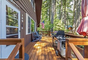 A wooden deck with a grill and chairs, overlooking a forested area. - Elk Country Cabin | Wood Stove, BBQ, EV Charger (Packwood)