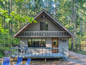 A cabin with a porch, numbered 157, surrounded by a forest.