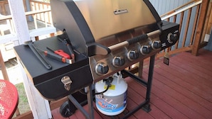 Una parrilla de gas portátil con cuatro quemadores, un estante lateral y un tanque de propano.