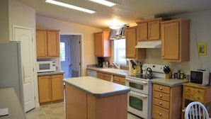 Una cocina con armarios de madera, un microondas, una estufa y un pequeño comedor con una silla.