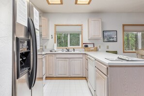 A modern kitchen with white cabinetry, a built-in refrigerator, a large window, and a view of the outdoors.