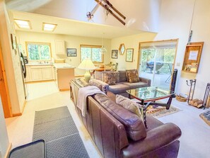 A living room with a sofa, a glass coffee table, and a kitchen area with cabinets and a window.