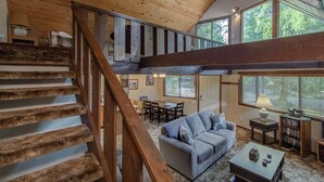 A spacious living area with a wooden staircase, a sofa, a coffee table, and a bookshelf. - Lake Creek Retreat| Mt Rainier, WiFi, Woodstove (Packwood)