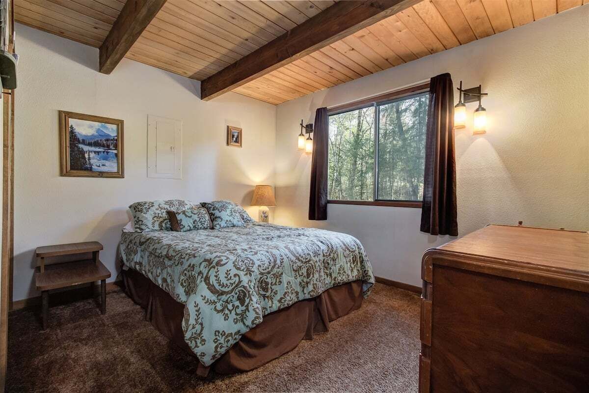Une chambre à coucher avec un lit, une table de chevet, une lampe, une commode et une fenêtre avec des rideaux.