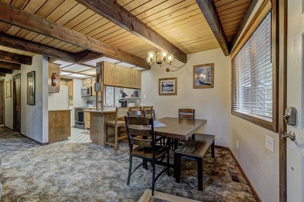 A cozy dining area with wooden furniture, a chandelier, and a view through a window with blinds. - Lake Creek Retreat| Mt Rainier, WiFi, Woodstove (Packwood)