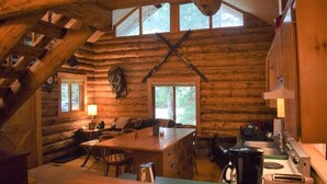 A log cabin interior with a dining area, kitchen, and a staircase.