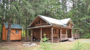 A rustic log cabin with a porch, surrounded by dense forest.