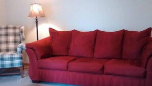 A red sofa, a plaid armchair, and a floor lamp in a room.