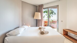 Une chambre d’hôtel avec un grand lit, une lampe de chevet, un banc en bois et une vue sur l’extérieur.