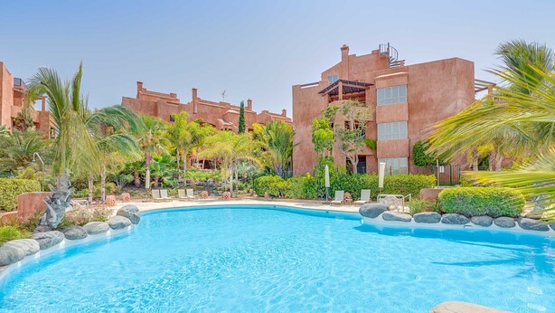 Une piscine entourée de palmiers et un bâtiment doté d’un toit plat.