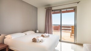 Une chambre d’hôtel avec un grand lit, une table de chevet, une lampe et une vue sur la plage, accessible par une porte-fenêtre coulissante.