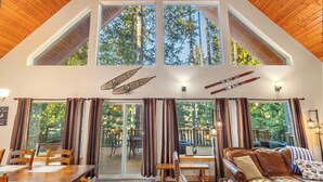 Ein Zimmer mit hohen Decken, großen Fenstern, einer Holzbalkendecke und Blick auf hohe Bäume.