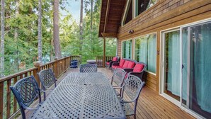 Eine Holzdielen-Terrasse mit Gartenmöbeln, einer Glastür und Blick auf einen Wald.