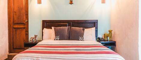 A neatly made bed with a striped bedspread, a wooden headboard, and two wall-mounted light fixtures.