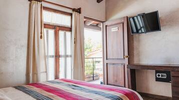A bedroom with a bed, curtains, a TV, a desk, and a door leading to an outdoor area.