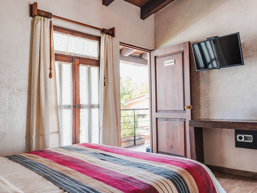A bedroom with a bed, curtains, a TV, a desk, and a door leading to an outdoor area.