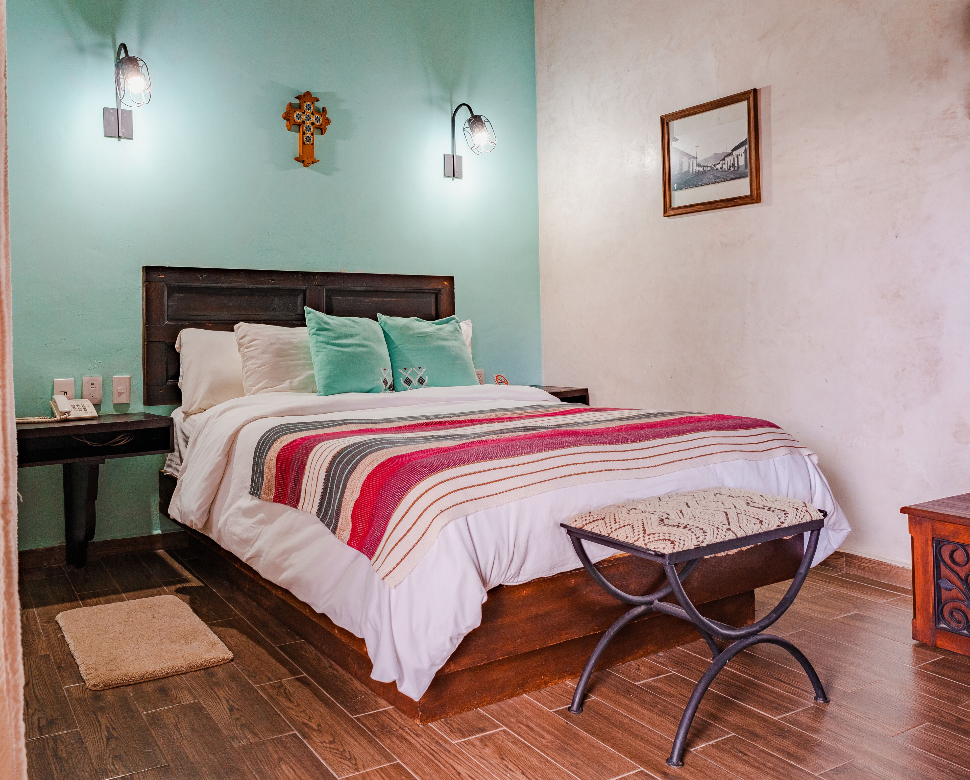 A neatly made bed with a striped blanket, a wooden nightstand with a phone, and a wall-mounted light fixture.