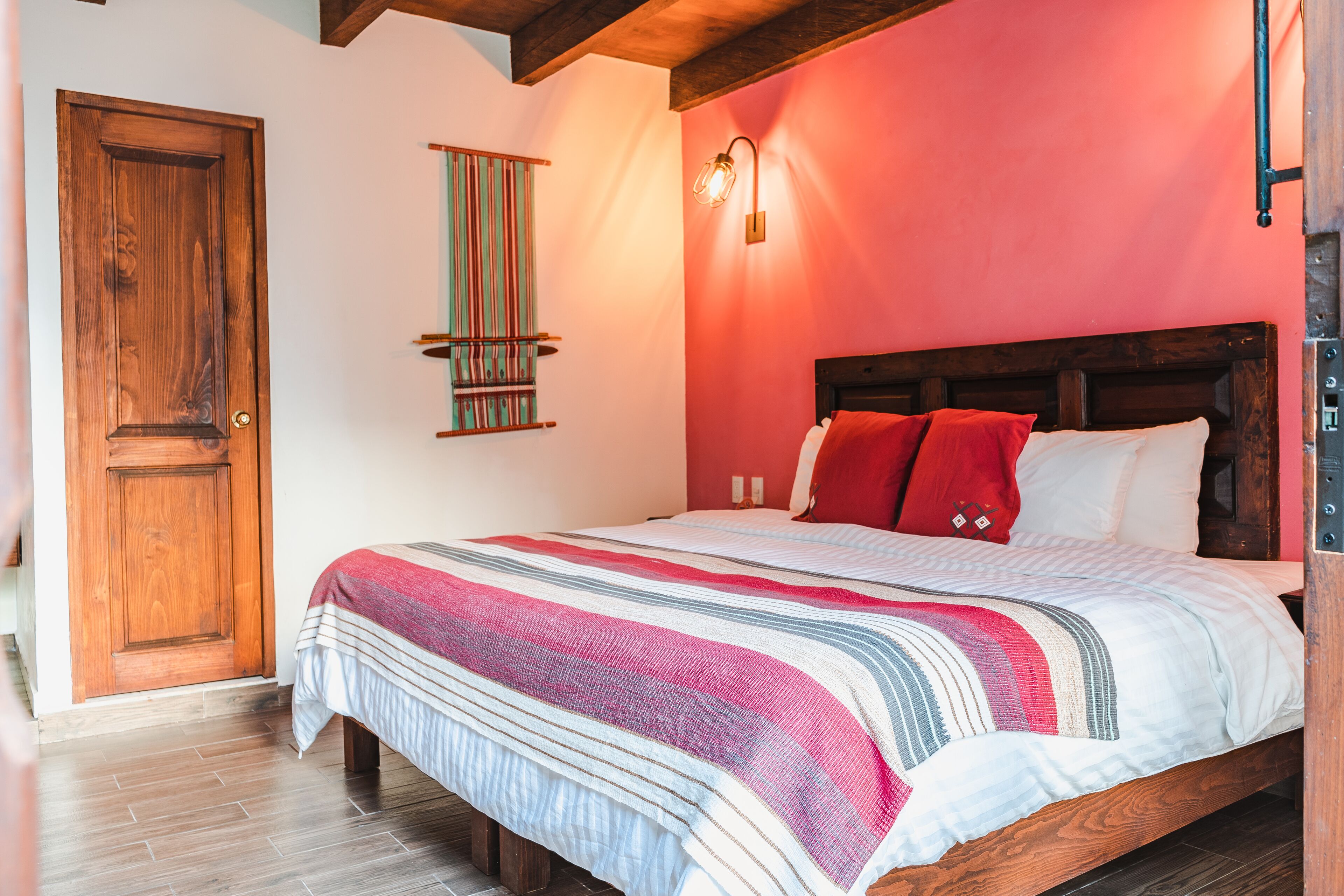 A bedroom with a wooden bed, a red wall, and a wooden door.