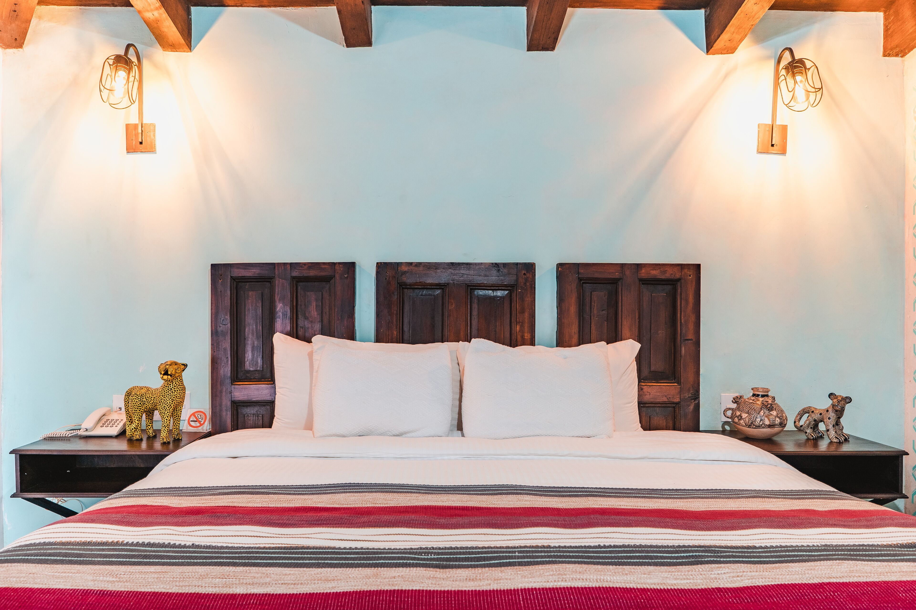 A bed with a striped blanket, two nightstands with decorative items, and wall-mounted lights.