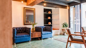 A cozy lobby with two blue armchairs, a wooden coffee table, and a bookshelf with decorative items. - Yox Hotel Boutique (San Cristóbal de las Casas)