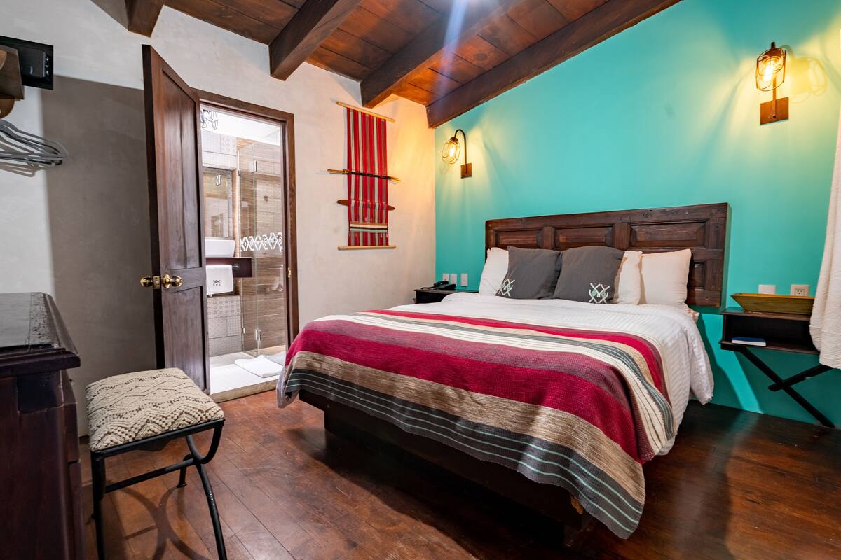 A bedroom with a wooden bed, a red and white striped blanket, a wooden nightstand, and a teal wall.